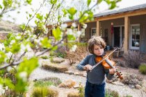 Шестилетний мальчик играет на скрипке возле своего дома — стоковое фото