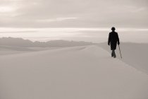 Hombre con un abrigo negro y un traje, un sombrero de jugador de bolos y un paraguas, en un desierto blanco desierto de arena blanca. - foto de stock