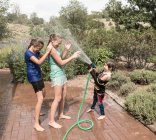 Bambini che si spruzzano a vicenda con tubo dell'acqua — Foto stock