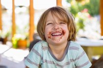 Retrato de sorrindo menino de 4 anos com chocolate em seu rosto brincando e rindo — Fotografia de Stock