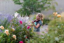 Teenagermädchen steht zwischen blühenden Rosen und Sträuchern und spielt Geige — Stockfoto