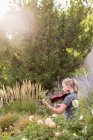 Девочка-подросток, стоящая среди цветущих роз и кустов, играющая на скрипке — стоковое фото