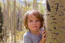 Retrato de niño de 4 años escondido detrás de un árbol de álamo - foto de stock