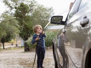 Четырехлетний мальчик моет машину на парковке — стоковое фото