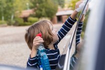 Чотирьохрічний хлопчик полірує автомобіль зовні з прибиральником і тканиною — стокове фото