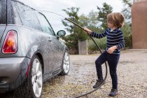 Ragazzo di quattro anni che lava un'auto usando un tubo flessibile — Foto stock