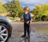 Vierjähriger Junge wäscht Auto mit Schlauch — Stockfoto
