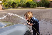 Menino de quatro anos lavando um carro usando uma mangueira — Fotografia de Stock