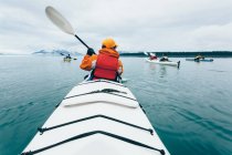 Una persona remando en un kayak de mar doble en aguas tranquilas frente a la costa de Alaska. - foto de stock