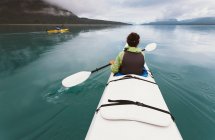 Sea kayaker extends paddle over her head, pristine waters of Muir Inlet in distance, Glacier Bay National Park, Alaska — Stock Photo