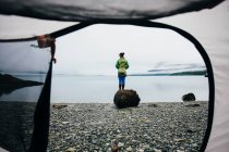 Vista através da porta da barraca de acampamento de mulher em pé na praia, uma entrada na costa do Alasca. — Fotografia de Stock