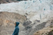 A young woman standing at the end of a glacier on a rocky shoreline in Alaska. — Stock Photo