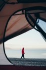 Vista attraverso la porta della tenda da campeggio di donna che cammina sulla spiaggia, Muir Inlet in lontananza, Glacier Bay National Park, Alaska — Foto stock
