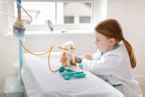 Young girl dressed as doctor pretending to treat toy dog in make-bleieve hospital bed — Stock Photo