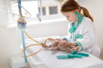Jeune fille habillée en médecin prétendant traiter câlin animal dans make-bleieve lit d'hôpital — Photo de stock