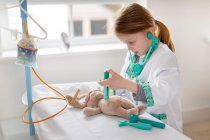 Giovane ragazza vestita da medico che finge di trattare il giocattolo coccoloso nel letto d'ospedale finto — Foto stock