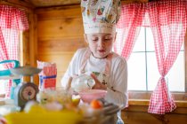 Jeune fille dans la maison wendy verser du lait prétendant cuisiner dans la cuisine — Photo de stock