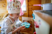 Young girl in wendy house putting cup cakes in oven pretending to cook in kitchen — Stock Photo