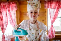 Portrait of young girl dressed in chef's outfit in wendy house pretending to cook in kitchen — Stock Photo