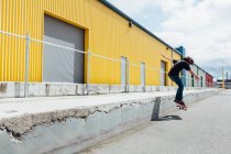 Teenage boy skateboarding in front of industrial warehouse loading zone — Stock Photo