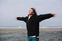 Adolescente en la playa con los brazos extendidos hacia la brisa, océano en la distancia - foto de stock