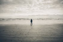 Adolescente de pé na vasta praia, ondas e céu nublado à distância — Fotografia de Stock