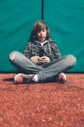 Хлопчик-підліток, що сидить на спортивному полі, тримає мобільний телефон — стокове фото