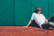Хлопчик-підліток, що сидить навпроти плетеної стіни на спортивному полі . — стокове фото