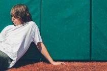 Adolescent garçon assis contre rembourré mur à terrain de sport. — Photo de stock