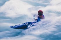 Long exposure of male whitewater kayaker paddling and surfing large rapids on a fast flowing river. — Stock Photo