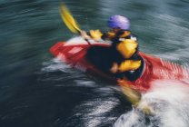 Lunga esposizione di femmina kayaker whitewater pagaiare rapide e navigare su un fiume che scorre veloce. — Foto stock