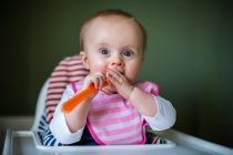 Portrait of baby girl holidng spoon sitting in high chair — Stock Photo