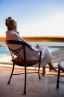 Mulher adulta sentada com uma bebida em uma varanda do hotel com vista para um oceano azul e praia de areia branca — Fotografia de Stock