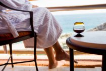 Adult woman sitting with a drink on a hotel balcony overlooking a blue ocean and white sand beach — Stock Photo