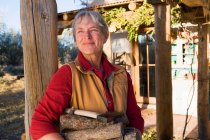 Mature woman at home on her property in a rural setting carrying logs — Stock Photo