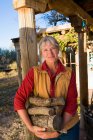 Mature woman at home on her property in a rural setting carrying logs — Stock Photo