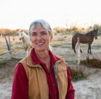 Зрелая женщина дома на своей территории в сельской местности, лошади в загоне — стоковое фото