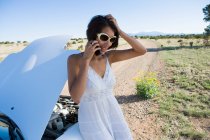 Mulher nativa americana em vestido de sol dirigindo um carro esporte conversível branco na estrada de terra do deserto com problemas de carro — Fotografia de Stock
