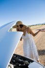 Корінна американська жінка в сонцезахисному одязі їздить білою кабріолет спортивною машиною на пустинній дорозі з автомобільними проблемами. — стокове фото