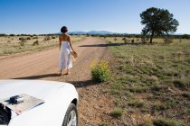 Mulher nativa americana em vestido de sol dirigindo um carro esporte conversível branco na sujeira do deserto — Fotografia de Stock