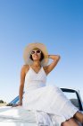 Корінна американська жінка в сонцезахисному одязі сидить на білій кабріолет спортивній машині. — стокове фото