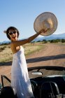 Коренная американка в солнечном платье водит белый кабриолет на грунтовой дороге пустыни — стоковое фото