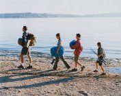 Family of four carrying camping gear, walking on beach at dusk — Stock Photo