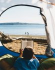 Мальчик читает книгу на открытии палатки на пляже. — стоковое фото