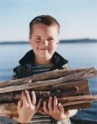 Portrait of happy young boy holding pile of firewood, — Stock Photo