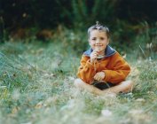 Boy sitting in field of tall grass, holding blade of grass — Stock Photo