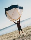 Mann hält ein kleines Kuppelzelt über dem Kopf, steht am Strand — Stockfoto