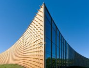 Современные университетские здания, деревянные балки, проектируемые из изогнутой деревянной облицовочной стены, на изогнутой поверхности земли — стоковое фото