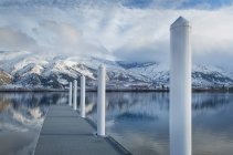 Piliers sur quai au lac près de la chaîne de montagnes enneigées — Photo de stock