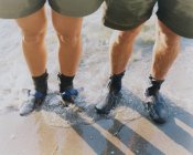 Man and woman wearing waterproof booties, standing in surf — Stock Photo